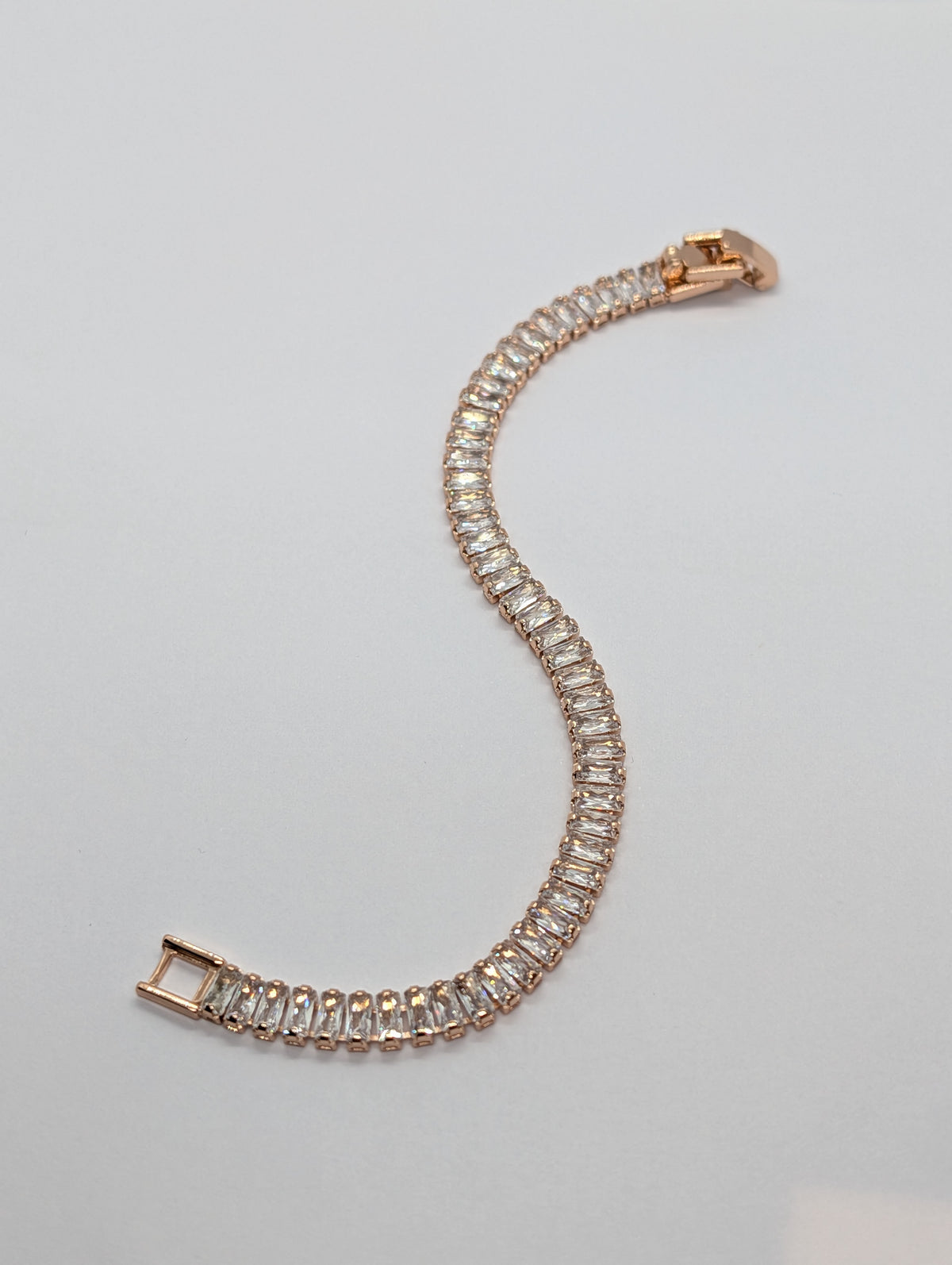 Rose gold baguette row tennis bracelet flat lay showing full length and fold-over clasp