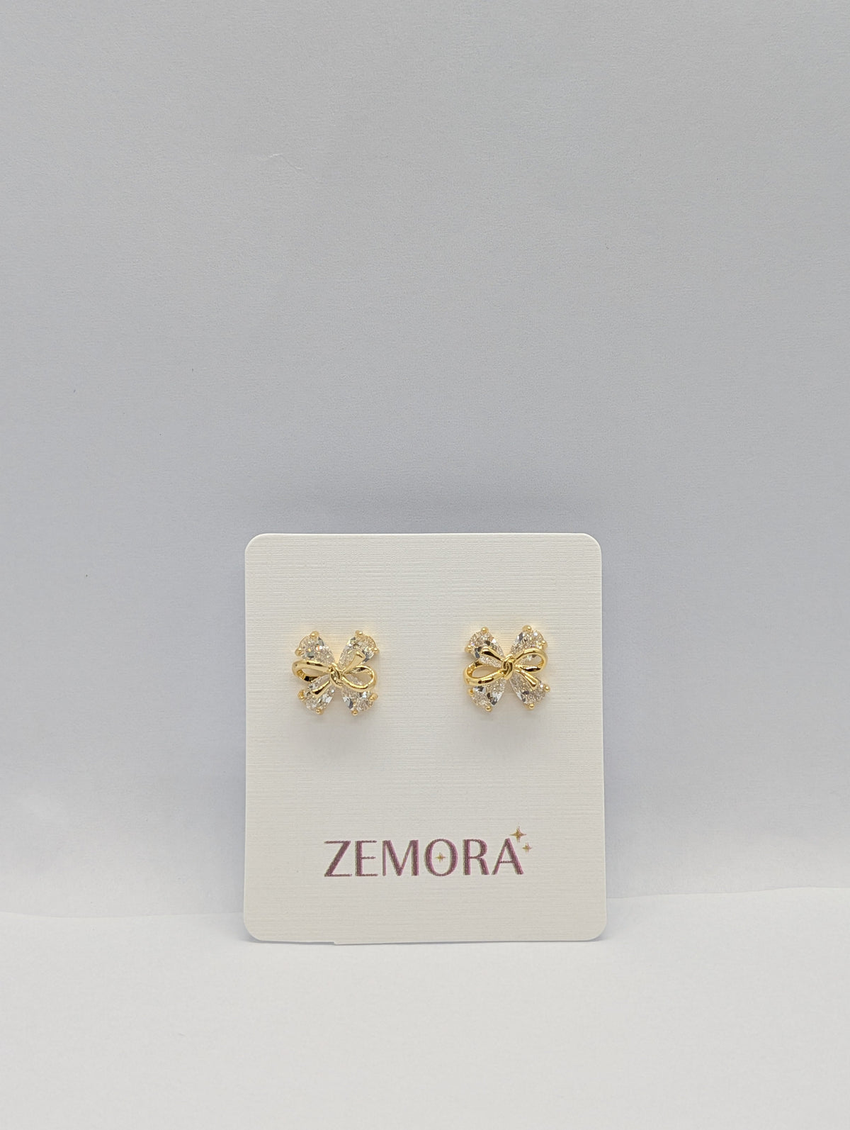 CZ Bow Stud Earrings - Gold tone pair on Zemora card display