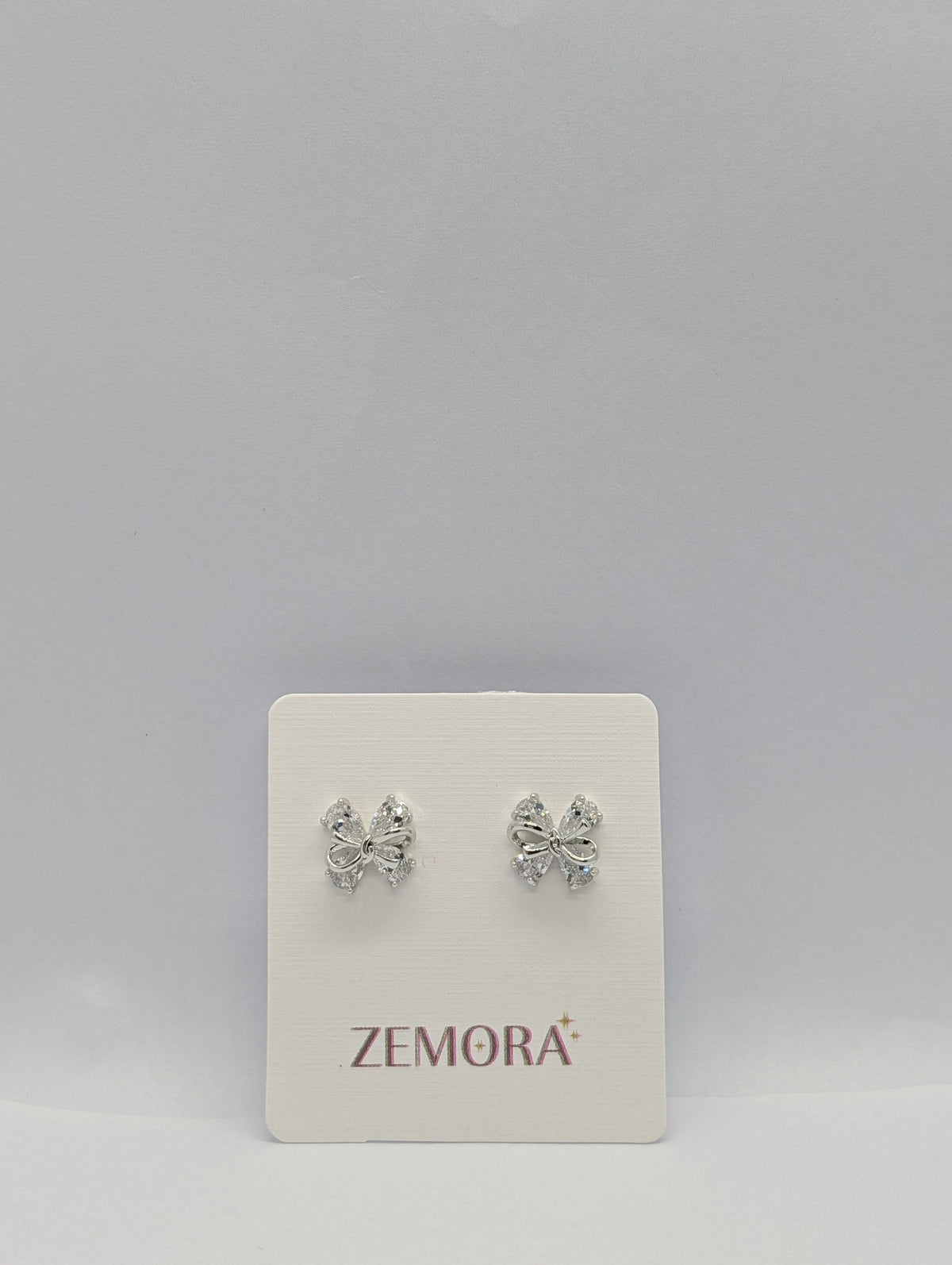 CZ Bow Stud Earrings - Silver tone pair on Zemora card display