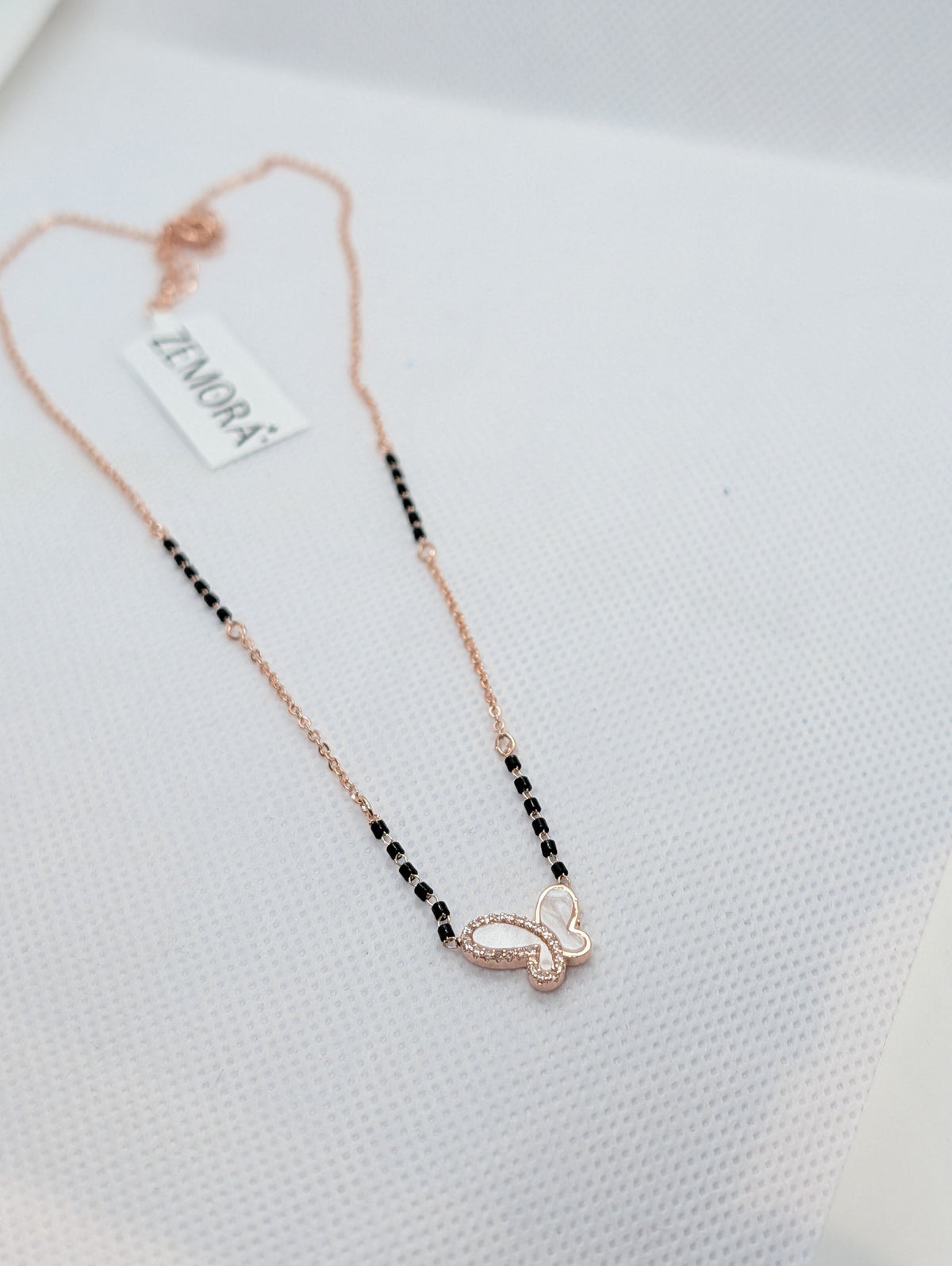 CZ Mother of Pearl Butterfly Mangalsutra - Gold tone pendant close up on white fabric