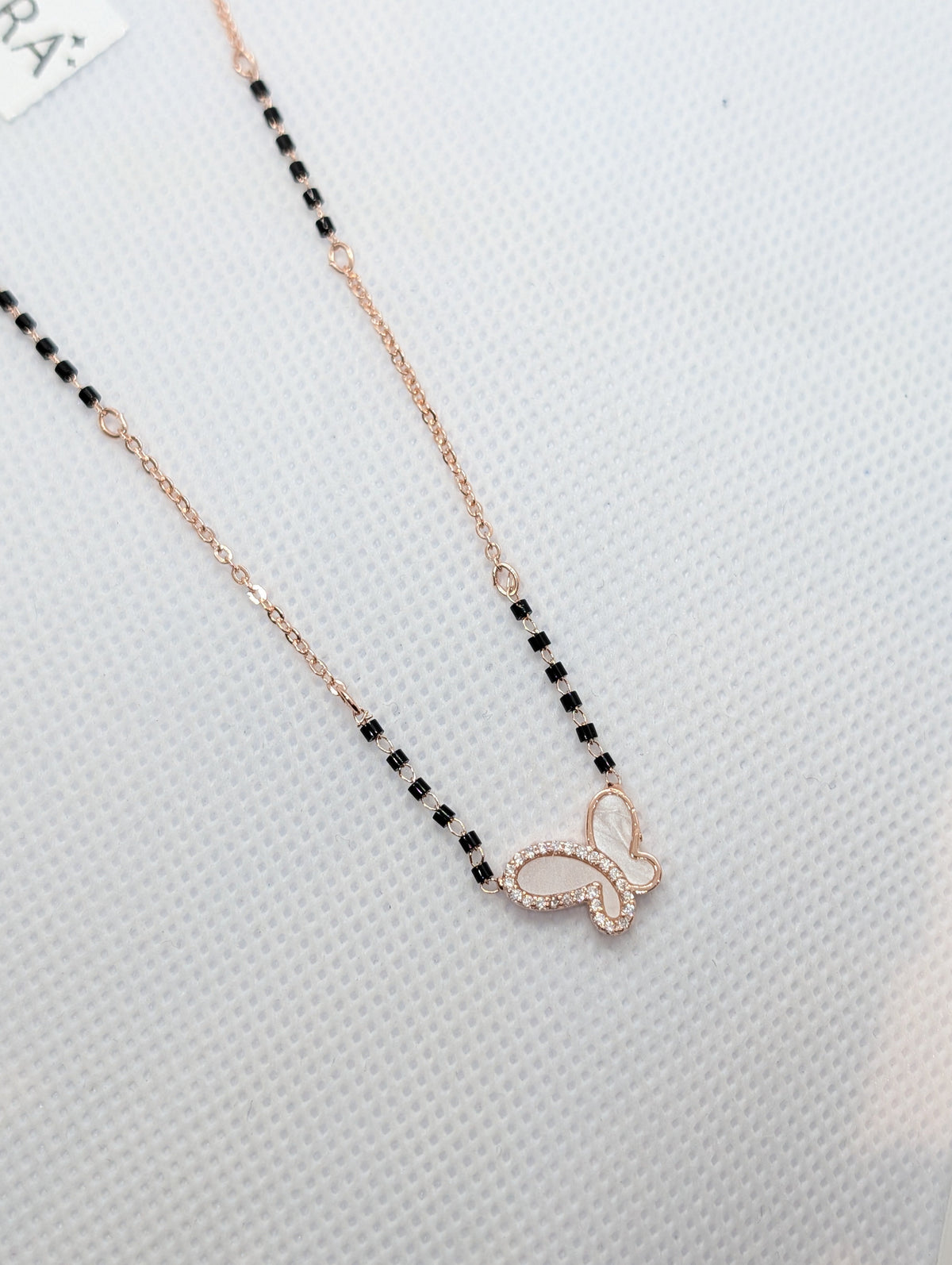 CZ Mother of Pearl Butterfly Mangalsutra - Gold tone angled flat lay on white fabric