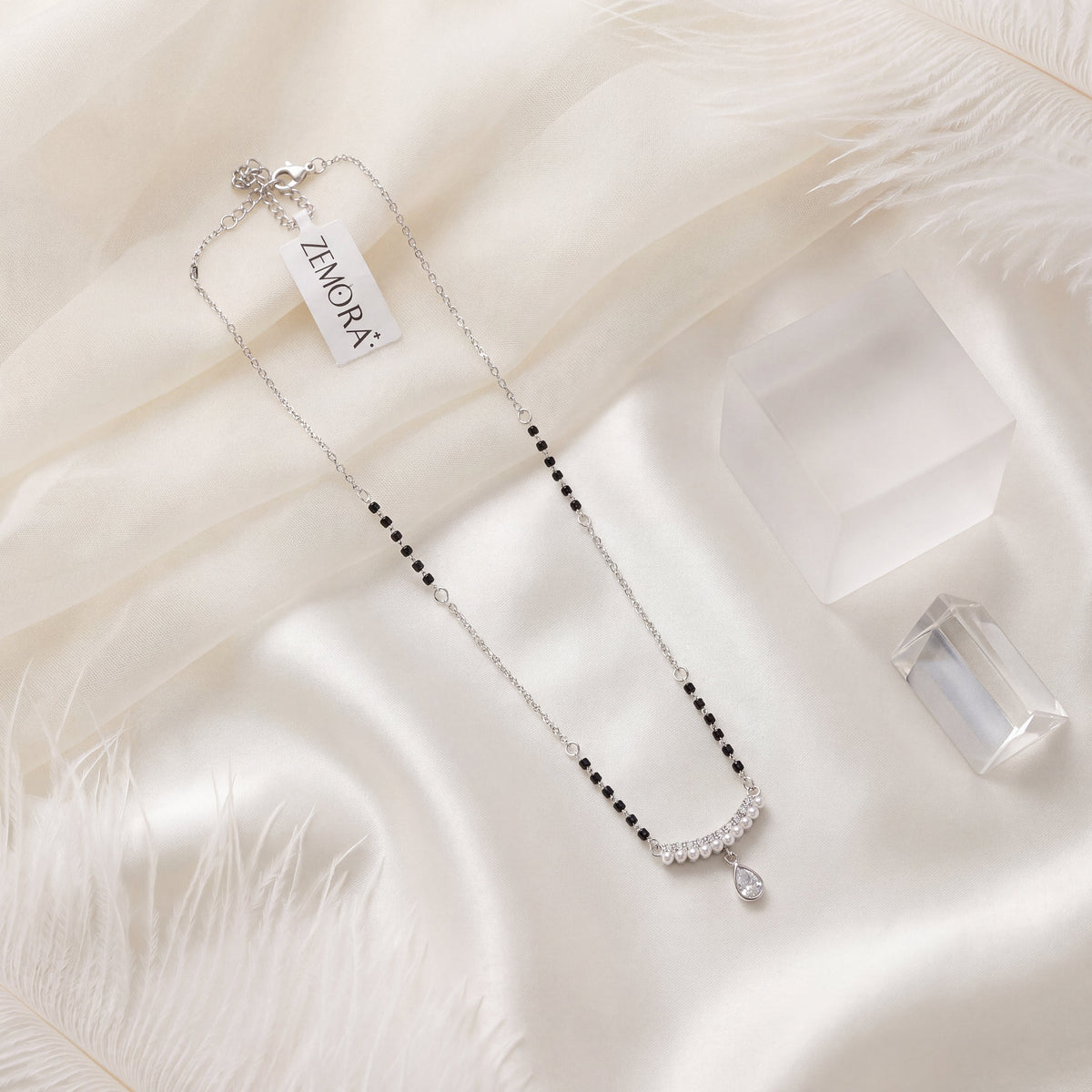 CZ Pave Arc Pearl Teardrop Mangalsutra - Silver tone lifestyle flat lay on white fur with Zemora tag and crystal