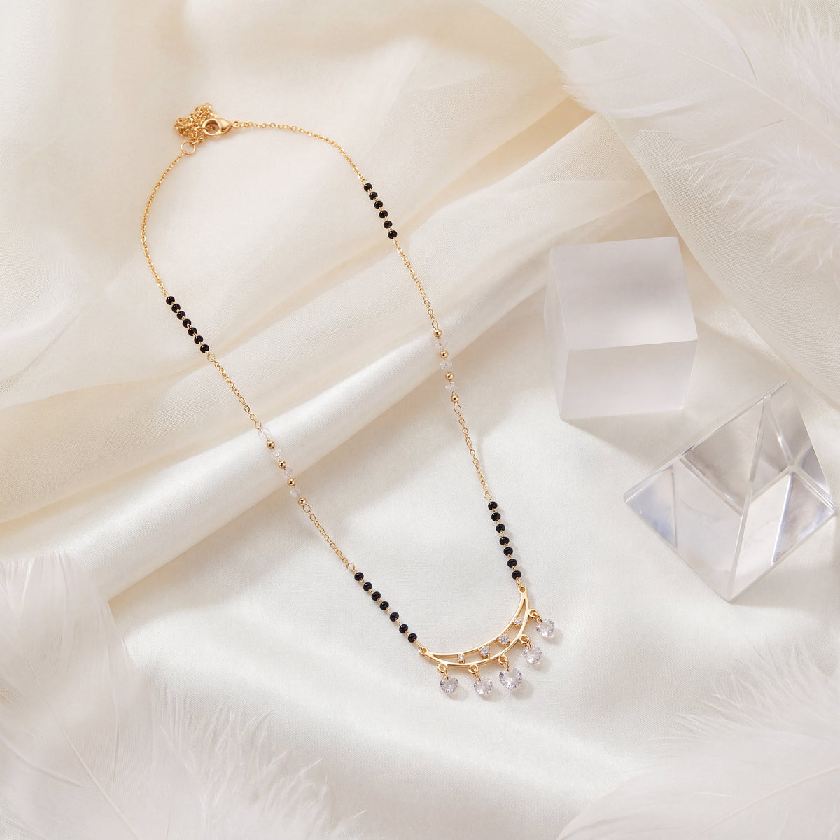 CZ Crescent Arc Multi-Drop Mangalsutra - Gold tone lifestyle flat lay on white silk with crystal accent