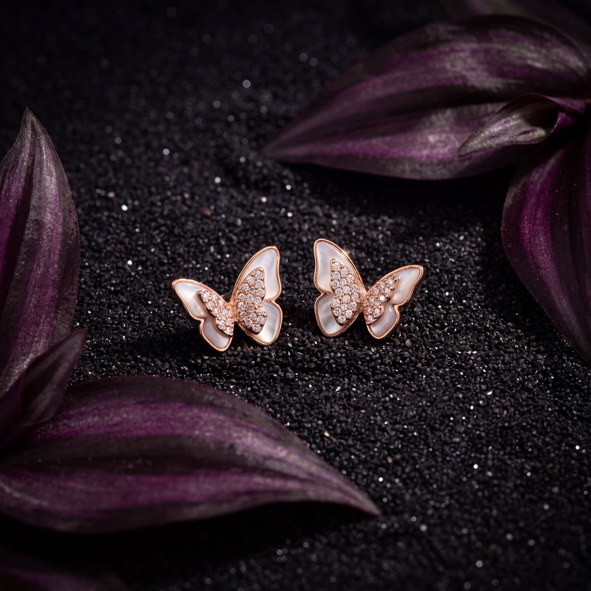 Mother of Pearl Pave CZ Butterfly Stud Earrings - Rose Gold lifestyle shot on dark background with purple leaves