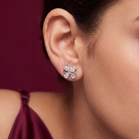 CZ Bow Stud Earrings - Silver tone worn on model ear with burgundy background close up