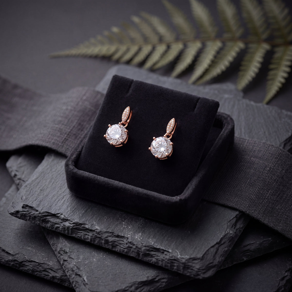 CZ Solitaire Drop Huggie Earrings - Rose Gold tone in black velvet jewellery box on dark slate with fern leaf lifestyle shot
