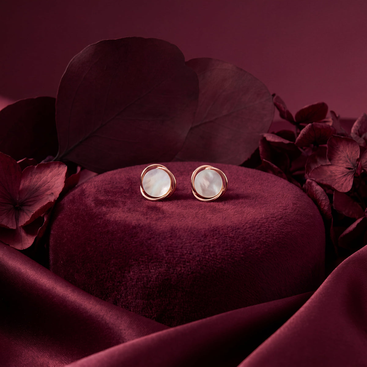 Mother of Pearl Wire Wrap Circle Stud Earrings - Rose Gold tone pair on burgundy velvet cushion with hydrangea petals lifestyle shot