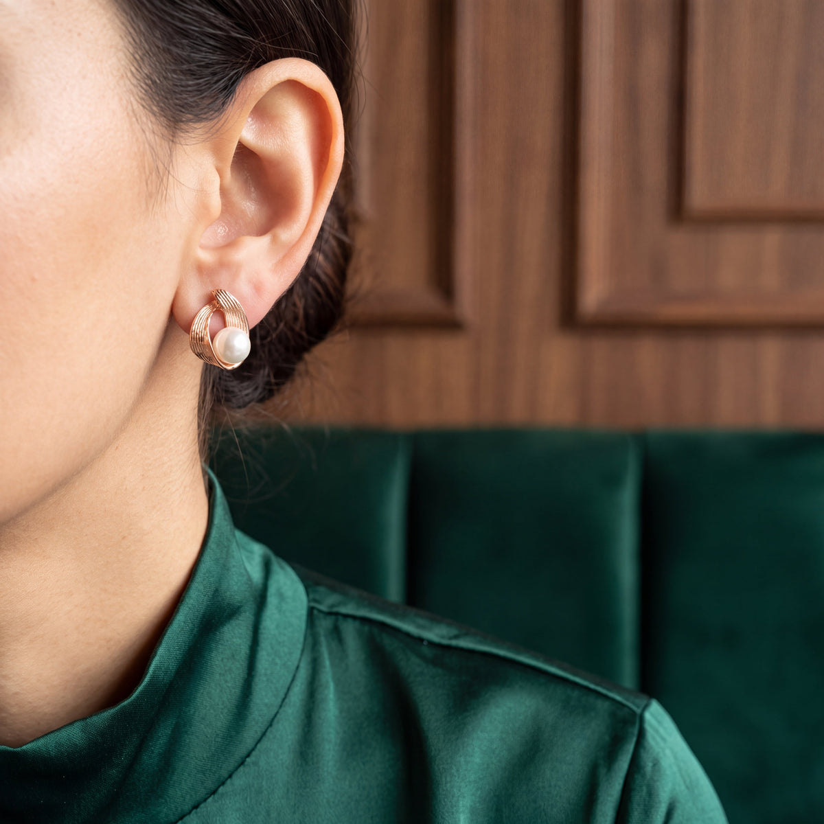 Pearl Ribbed Wire Wrap Stud Earrings - Rose Gold tone worn on model ear with teal silk shirt and wooden panel background