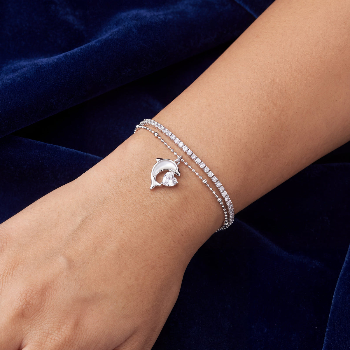 CZ Dolphin Charm Double Layer Bracelet - Silver tone worn on wrist against navy blue velvet background