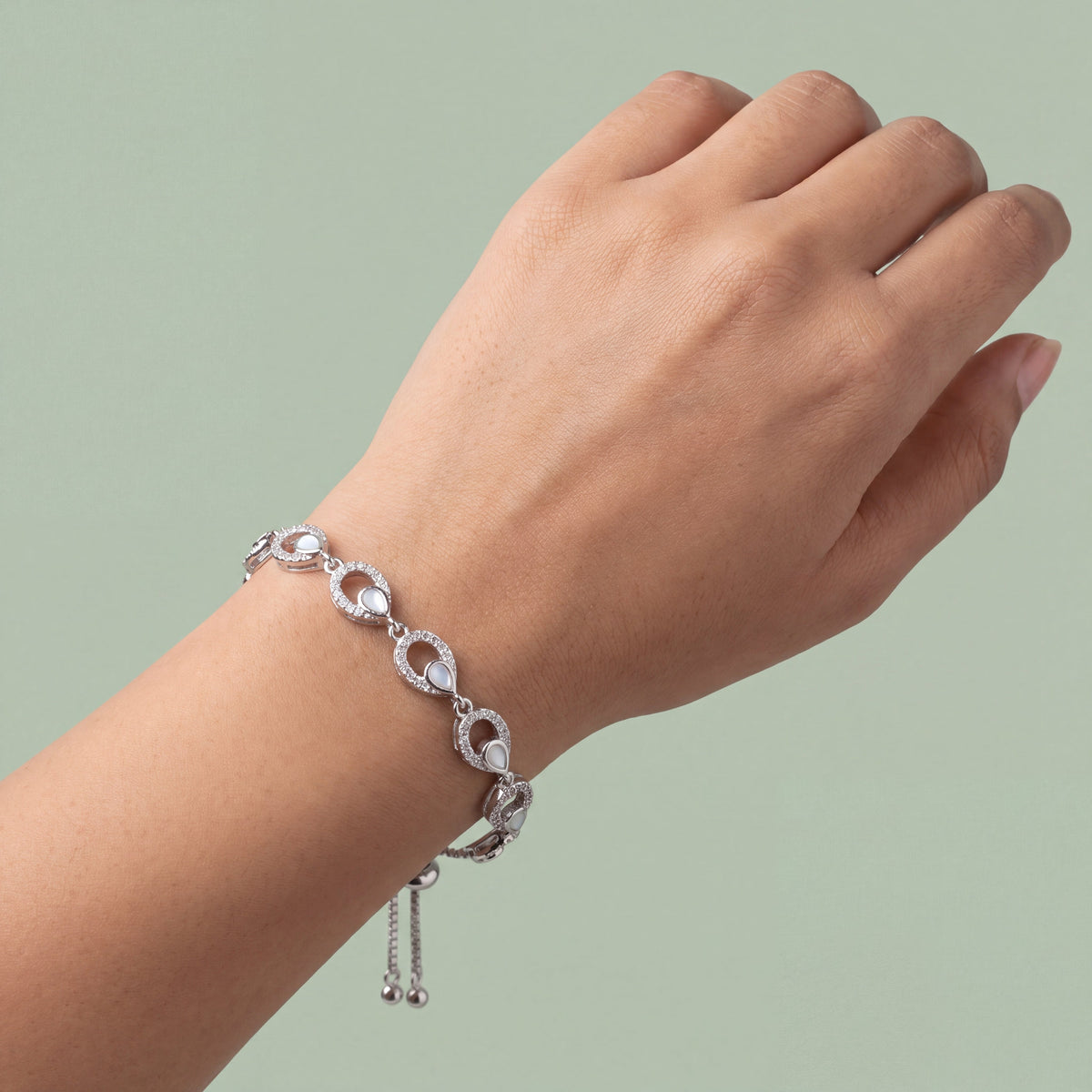 CZ Mother of Pearl Teardrop Link Bracelet - Silver tone worn on wrist against sage green background